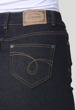 Jeans in denim blu scuro con cuciture gialle, un'etichetta in pelle KOROSHI e un design unico delle tasche curve sul retro.