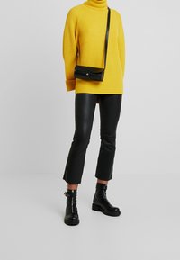 Žlutý žebrovaný rolák, černé kožené zkrácené kalhoty a černé kotníkové boty. Černá přes rameno taška s detailním stříbrným knoflíkem.