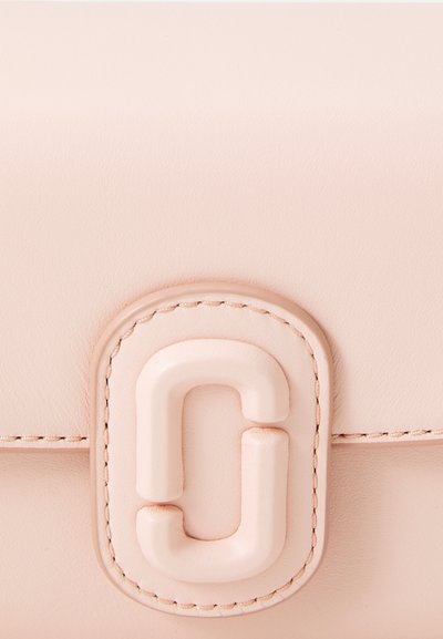 Lichtroze leren pouch met een textuurafwerking, voorzien van een opvallende sluiting in de vorm van een gestileerde letter "C" en bijpassende stiksels.