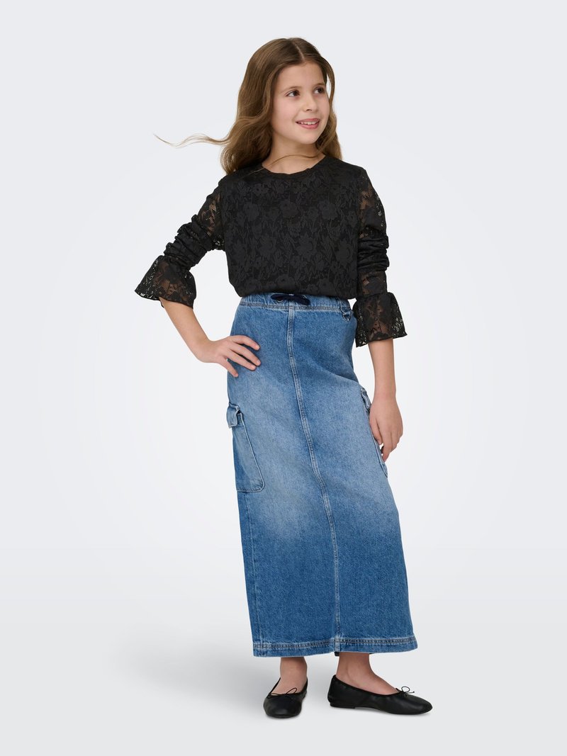 Juodas nėriniuotas ilgomis rankovėmis megztinis su raukiniais rankogaliais, derinamas su ilgu džinsiniu sijonu su šoninėmis kišenėmis. Komplektą papildo juodi lygūs batai.