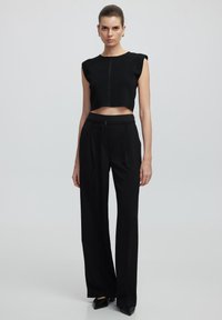 Černý cropped top s krátkými rukávy, se středovým švem. V kombinaci s černými kalhotami s vysokým pasem a černými špičatými botami.