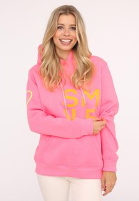 Helles rosa Hoodie mit gelbem "SMILE"-Text, Kängurutasche und Kordeln. Hergestellt aus weichem Stoff mit gerippten Bündchen und Saum.