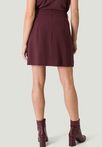 Jupe bordeaux avec une taille cintrée et une fermeture éclair à l'arrière. Fabriquée en tissu lisse, elle présente une coupe ajustée et tombe au-dessus du genou.