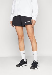 Svart trening shorts med hvit Adidas-logo, paret med hvite crew sokker med svarte striper, og svarte trening sko med mesh-design.