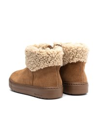 Botas tobilleras de ante marrón con un suave puño de borrego beige, suela de goma y detalles de costura en los lados. Apariencia texturizada y acogedora.