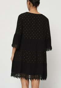 Robe noire à trois niveaux, ornée de motifs de points dorés et de dentelle au bas et aux manches. Fabriquée en tissu léger, au design ample.