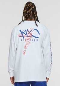 Weißes langärmeliges Hemd mit einem Grafikdruck eines Basketballspielers in Orange vor blauen "K1X"- und "PLAY HARD"-Text auf der Rückseite.