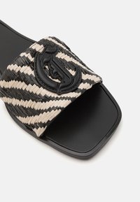 Sandalo a fascia intrecciata con un motivo a strisce nere e beige, caratterizzato da un emblema nero prominente sulla parte superiore e una suola nera elegante.
