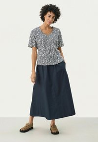 Top a maniche corte, stampato in blu navy e bianco con scollatura a V, abbinato a una gonna lunga blu scuro e sandali beige con lacci.