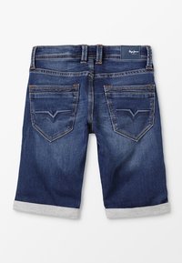 Denimshorts i mörkblått med uppvikt nederkant. Har två bakfickor med en subtil V-formad design och en etikett vid midjan.