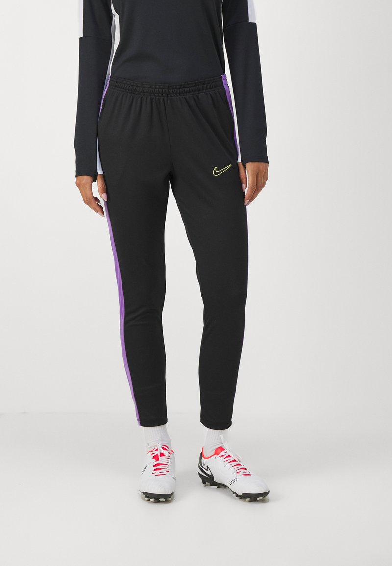 Pantalones deportivos negros con franjas laterales moradas, cintura elástica y un pequeño logotipo de Nike amarillo en el muslo. Material suave y elástico.