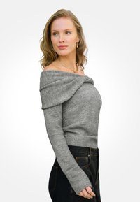 Szary sweter odsłonięty na ramionach z długimi rękawami i prążkowanym wykończeniem, wykonany z miękkiego materiału dzianinowego; zestawiony z czarnymi spodniami z detalami przeszycia.