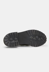 Suola di scarpe in gomma nera con un motivo di battistrada robusto, caratterizzato da scanalature profonde e accenti rialzati per una maggiore trazione. La taglia indicata è 37.