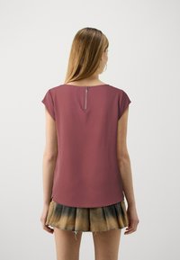 Kurzarmoberteil in Mauve mit einem verdeckten Reißverschluss auf der Rückseite. Der Stoff ist glatt und leicht strukturiert. Kombiniert mit einem plissierten Rock in einem Farbverlauf.