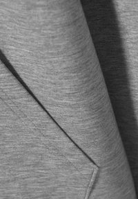 Harmaa kangas, jossa on pehmeä rakenne, sisältää viistosti taitoksia ja tasaisen, kirjavan pinnan, joka korostaa erilaisia harmaan sävyjä.