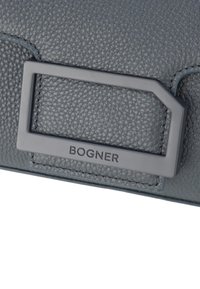Borsa in pelle grigia con texture, caratterizzata da una hardware a logo rettangolare con la scritta "BOGNER". Il design è elegante con dettagli di cucitura visibili.