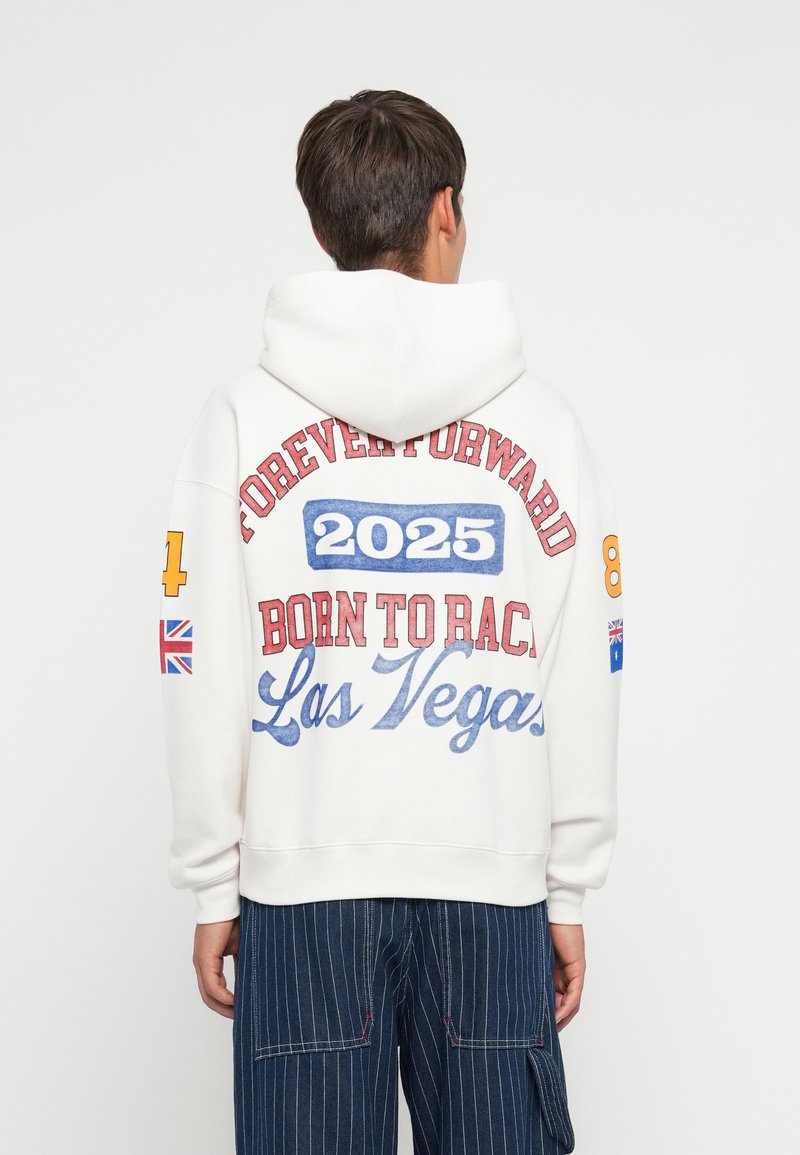 Moletom branco com texto colorido: "PARA SEMPRE PARA A FRENTE," "2025," "NASCIDO PARA CORRER," e "Las Vegas." Inclui bandeiras e acentos em negrito; tecido suave.