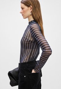 Top trasparente a maniche lunghe con righe orizzontali nere e blu, design con collo alto, abbinato a pantaloni neri a vita alta e una borsa nera a mano.