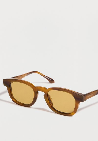 Lunettes de soleil rectangulaires translucides marron avec des verres ambrés, posées sur une surface blanche, avec le logo Giorgio Armani visible sur la branche.
