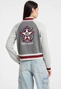 Maglione grigio e grigio chiaro con righe rosse e bianche sulla parte a coste, caratterizzato da una grande stella rossa e il logo "G" sul retro, realizzato in tessuto lavorato a maglia.