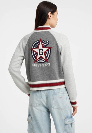 Maglione grigio e grigio chiaro con righe rosse e bianche sulla parte a coste, caratterizzato da una grande stella rossa e il logo "G" sul retro, realizzato in tessuto lavorato a maglia.