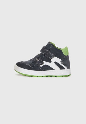 Chaussures montantes pour enfants en suede bleu marine avec des accents blancs, un col vert et des sangles Velcro. Elles possèdent une semelle en caoutchouc blanche.