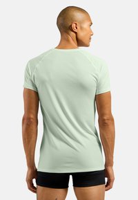 Mint green, short-sleeve active t-shirt with a smooth texture and raglan sleeves, viewed from the back, paired with black shorts.