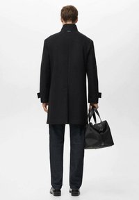 Czarny wełniany płaszcz z wysokim kołnierzem, prostego kroju i zapinanymi na guziki mankietami, w połączeniu z ciemnymi dżinsami i czarną torbą na ramię.