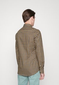 Langärmeliges Hemd mit einem Hahnentrittmuster in Schwarz, Gold und Weiß, mit einem klassischen Kragen und Knopfmanschetten, kombiniert mit mintfarbenen Hosen.