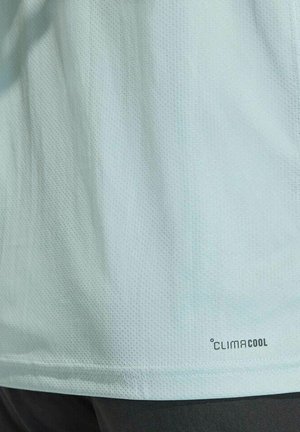 Chemise en tissu bleu clair texturé avec un petit logo "CLIMACOOL" près de l'ourlet, au-dessus d'un pantalon sombre.