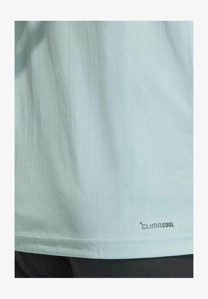 Chemise en tissu bleu clair texturé avec un petit logo "CLIMACOOL" près de l'ourlet, au-dessus d'un pantalon sombre.