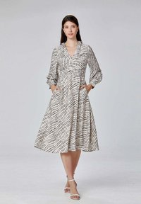 Robe longueur genoux, style portefeuille en tissu léger, avec un motif à carreaux noirs sur fond blanc ; manches longues bouffantes et poches latérales.