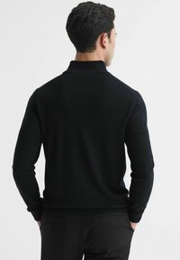 Pulover din tricot negru cu guler, având mâneci lungi și tiv ribatat, expus din spate pe un fundal deschis.
