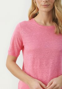 Rövid ujjas, kerek nyakú póló világos rózsaszínben, puha, texturált anyagból, enyhén melírozott kivitelben. Egyszerű dizájn, minta nélkül.