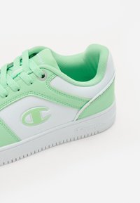 Sneaker verde menta e bianca con parte superiore in sintetico testurizzato, collo imbottito, lacci tondi e suola in gomma con scanalature per la trazione.