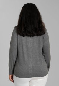 Grau pullover mit langen Ärmeln, rundem Halsausschnitt und geripptem Saum. Weicher Stoff, taillierte Passform und minimale Details. Weiße Hose am unteren Rand sichtbar.