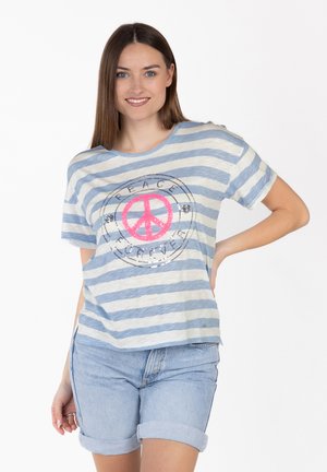 Jeune femme souriante, portant une chemise rayée bleue et blanche avec un symbole de paix rose et le texte "Peace Forever", associée à un short en denim clair.