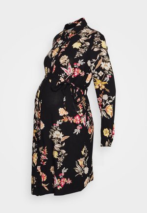 Robe de maternité noire à fleurs avec manches longues, taille ceinturée et col à revers, arborant des motifs floraux colorés et un tissu doux.