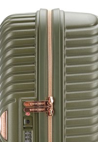 Nahaufnahme eines olivgrünen Hartschalenkoffers mit geriffelter Textur, Reißverschlüssen in Roségold und eingebautem TSA-Kombinationsschloss.