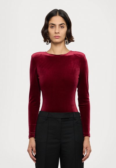 Langärmliger Bodysuit aus tiefburgunder Samt mit glatter Textur, ergänzt durch maßgeschneiderte schwarze Hosen, mit einem runden Ausschnitt.