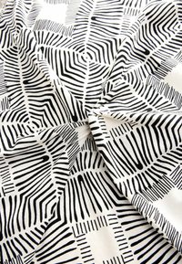 Stoff mit schwarz-weißer Musterung, der unregelmäßige, kräftige Linien und Formen auf einer glatten, leichten Baumwolltextur zeigt.