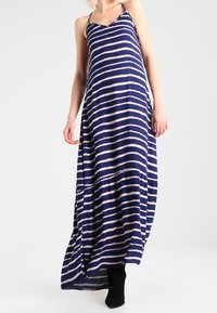 Randig maxiklänning i marinblå och krämfärgad, tillverkad av lättviktsmaterial med V-ringning och justerbara remmar, med en flödande siluett.