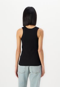 Svart ribbestrikket tank topp med en tettsittende design, rund halslinje og uten ermer, sammen med lyseblå høyhårede jeans.
