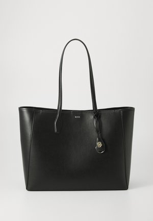 Sac fourre-tout en cuir noir avec deux longues poignées, une texture lisse, et une étiquette logo en accent doré. Forme rectangulaire avec un design à ouverture ouverte.