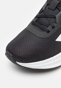 Black athletic shoe with a textured mesh upper, smooth synthetic accents, and a white midsole. Features black laces and a reinforced toe.