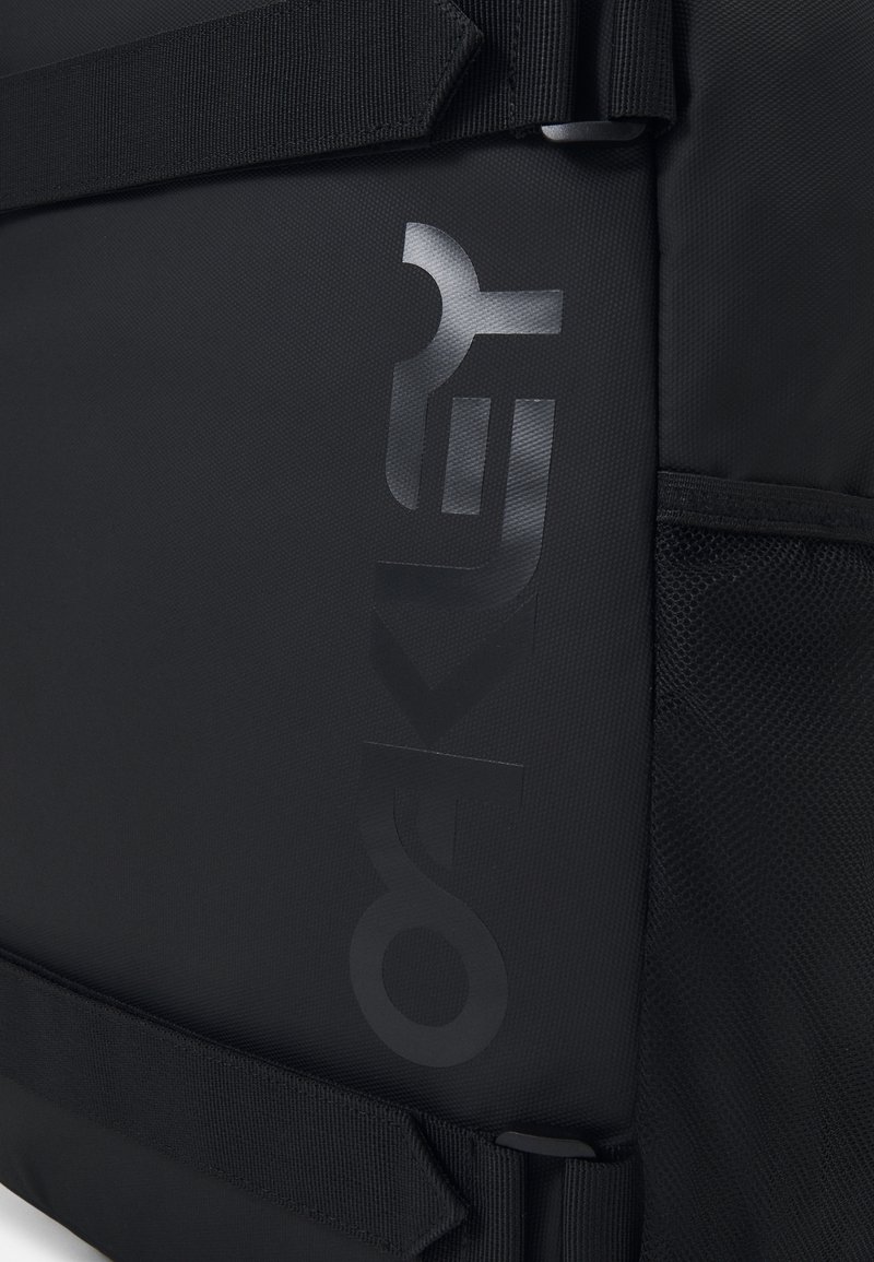 Black backpack featuring a textured exterior, mesh side pocket, and a prominent embossed logo. Adjustable straps visible on top.