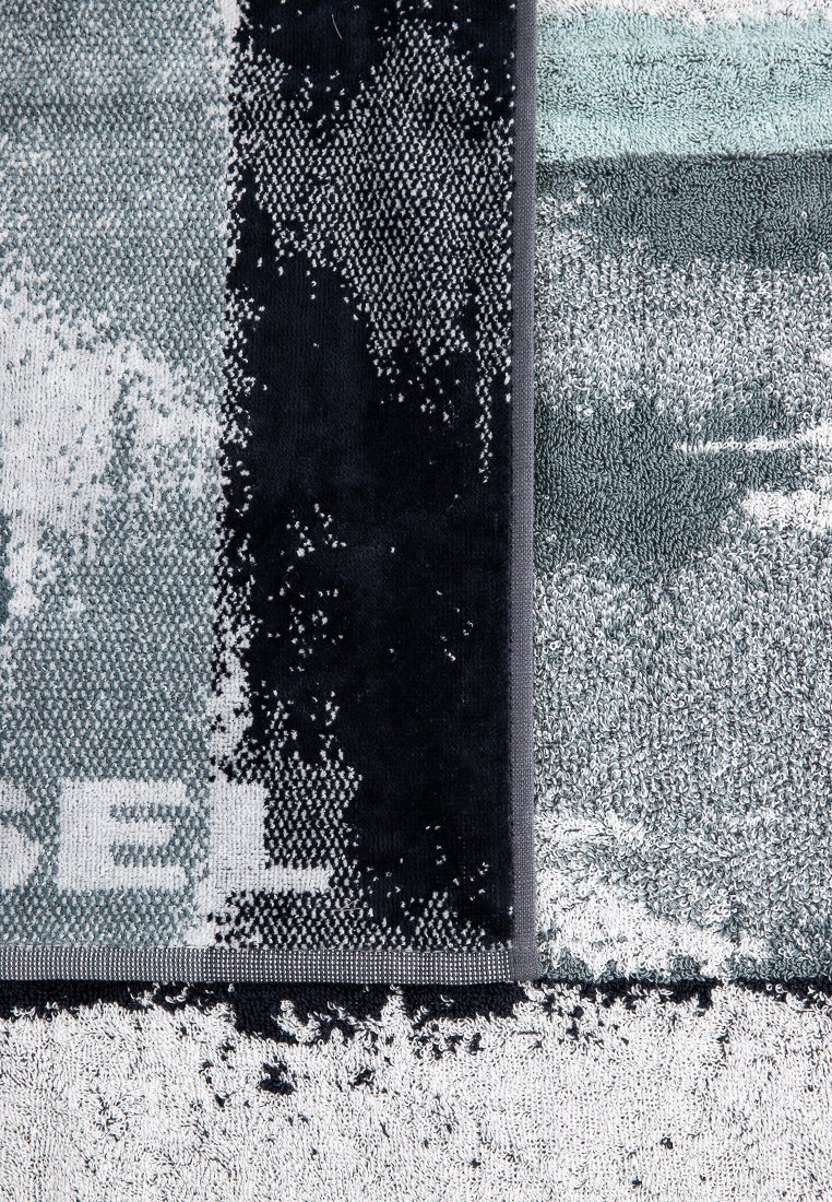 Ciemny i jasny ręcznik o teksturze z geometrycznym wzorem, z mieszanką kolorów szarego, czarnego i turkusowego, wykończony szarym brzegiem.