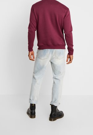 Felpa bordeaux con polsini e fondo a coste, abbinata a jeans blu chiaro con orli arrotolati, stivaletti neri alla caviglia con suola spessa.