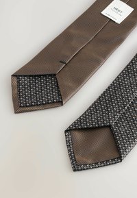 Deux cravates : l'une en tissu texturé marron avec un motif subtil, et l'autre avec une doublure à motifs foncés ; les deux ont une coupe triangulaire aux extrémités.