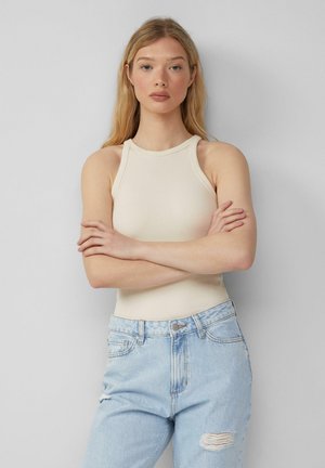Cream ribbed tank top with a high neckline, paired with light blue distressed jeans featuring a ripped knee. Smooth texture, fitted design.